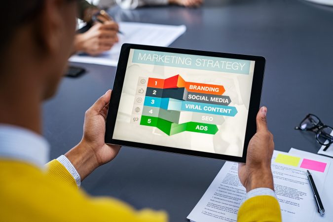 Close up of young man using digital tablet to study marketing strategy. African businessman studying business planning. Rear view of student holding tablet in hands and analyze business material on screen.