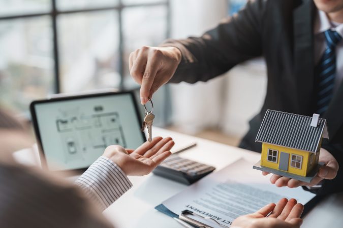 Real estate agent gives the couple the keys to the house after they sign the real estate sale contract. House and real estate trading concept.