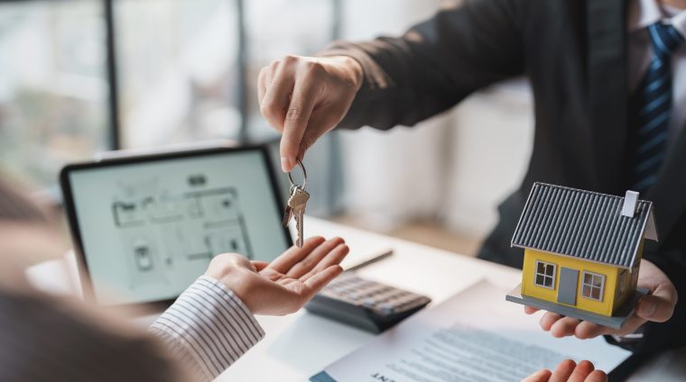 Real estate agent gives the couple the keys to the house after they sign the real estate sale contract. House and real estate trading concept.