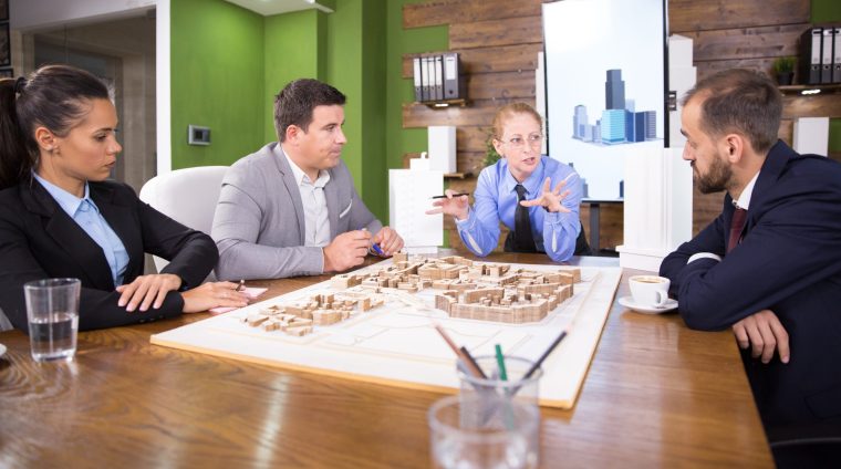 Middle age real estate developer in a meeting with construction engineers. Mini town. Building model.