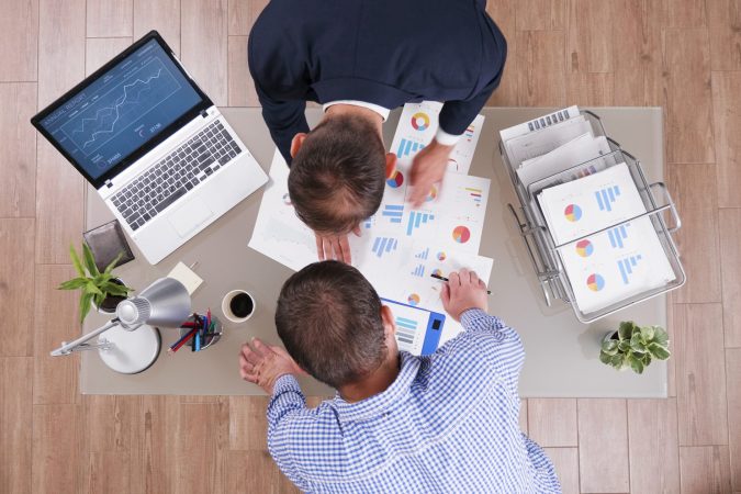 Top view of businessman analyzing management graphs discussing company strategy during businessmeeting in startup corporate office. Partners working at investments presentation during partnership