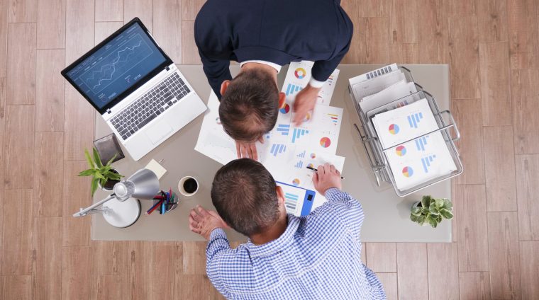 Top view of businessman analyzing management graphs discussing company strategy during businessmeeting in startup corporate office. Partners working at investments presentation during partnership